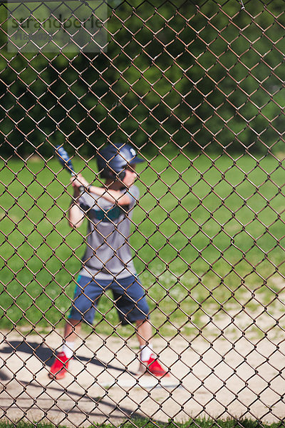 Blick durch den Maschendrahtzaun eines Baseball spielenden Jungen