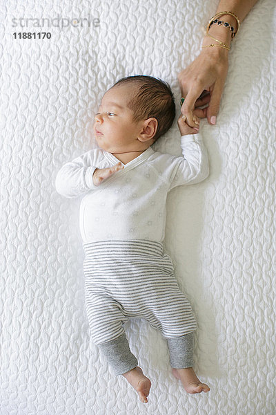 Junge liegt auf dem Bett  Mutter hält die Hand des Babys  Draufsicht