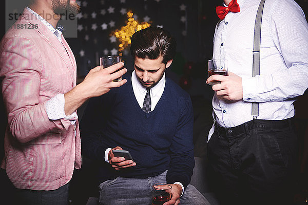 Drei Männer auf der Party  der Mann in der Mitte benutzt ein Smartphone