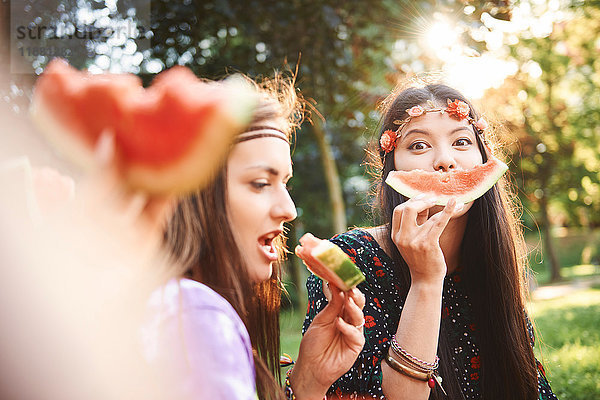 Junge Boho-Frauen machen auf dem Festival ein Smiley-Gesicht mit Melonenscheibe