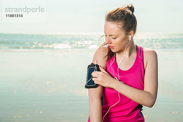 Junge Frau mit Kopfhörern am Strand beim Einstellen der Musik auf der Armbinde  Folkestone  UK