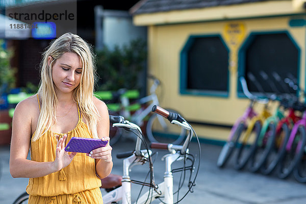 Junge Frau mit langen blonden Haaren schaut mit dem Fahrrad auf ein Smartphone  Santa Monica  Kalifornien  USA