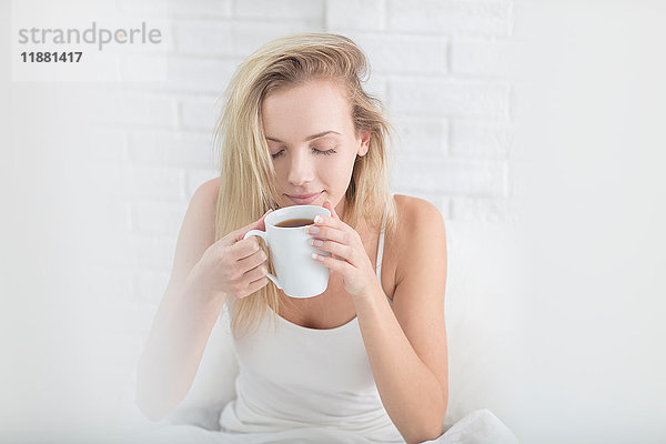 Junge Frau hält Kaffeetasse  Augen geschlossen  wacht langsam auf
