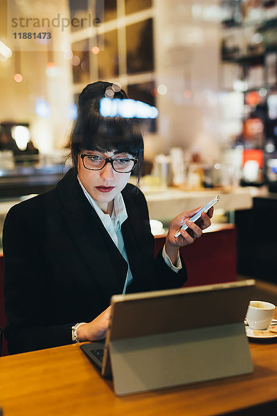 Geschäftsfrau benutzt Mobiltelefon und digitales Tablet im Cafe