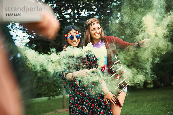 Junge Boho-Frauen tanzen mit grüner Rauchfahne auf dem Festival