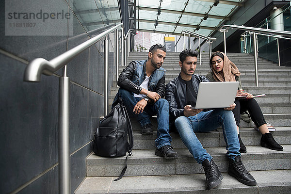 Drei Freunde  die auf Stufen sitzen und auf den Laptop schauen