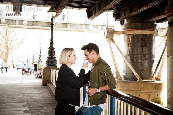Junges Paar  steht unter der Brücke  junge Frau berührt das Gesicht des Mannes  lächelt