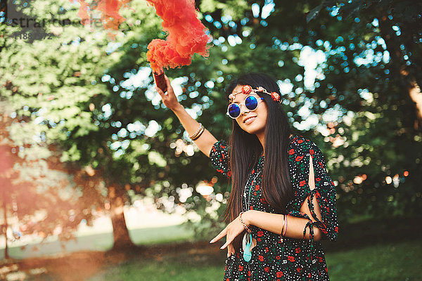 Junge Boho-Frau hält rote Rauchfackel beim Festival hoch