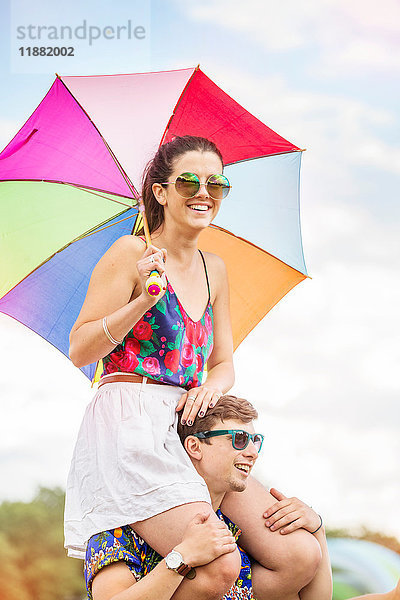 Mann trägt Frau mit Regenschirm auf den Schultern