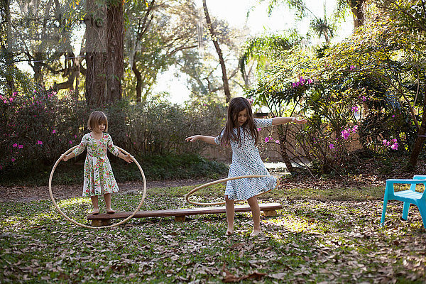 Zwei Schwestern spielen mit Plastikreifen im schattigen Garten