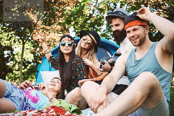 Fünf junge erwachsene Freunde spielen Akustikgitarre beim Festival-Camping