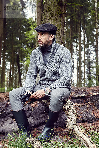 Mann in Freiluftkleidung  der aus einem Waldblock herausschaut