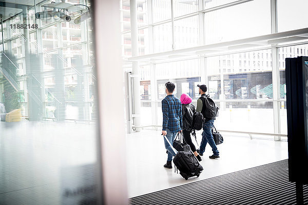 Drei Freunde  Spaziergang im Freien  Koffer auf Rädern ziehen  Rückansicht