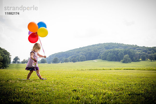 Mädchen geht mit einem Haufen bunter Luftballons über ein ländliches Feld