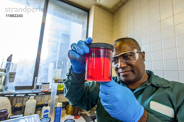 Laborantin betrachtet Becher mit rotem Biokraftstoff im Labor für Biokraftstoffanlagen