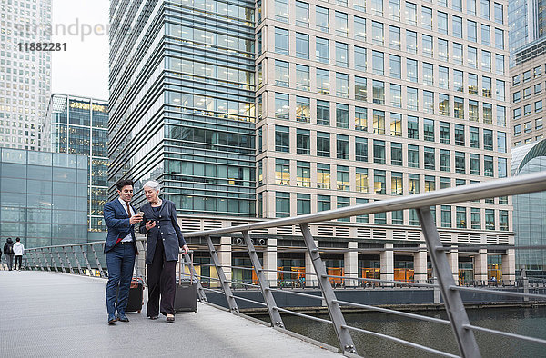 Geschäftsmann und Geschäftsfrau  die ein Mobiltelefon benutzen und Gepäckwagen ziehen  Canary Wharf  London  Großbritannien