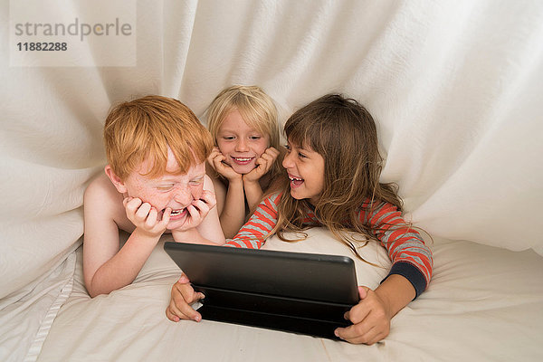 Kinder liegen im Bett und schauen auf das digitale Tablett