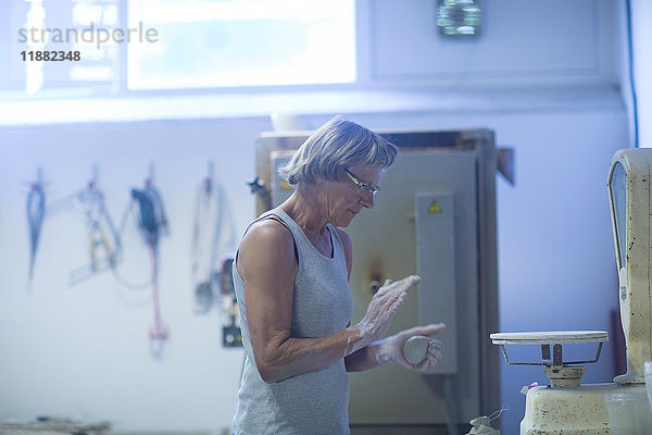Ältere Frau in Töpferwerkstatt  wiegt Ton für Töpferprojekt