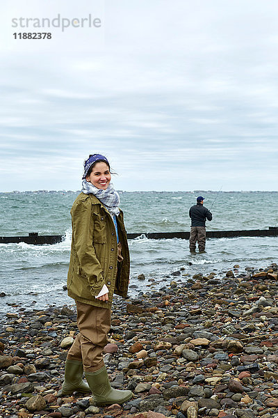 Porträt einer jungen Frau am Strand  während ihr Freund im Meer fischt