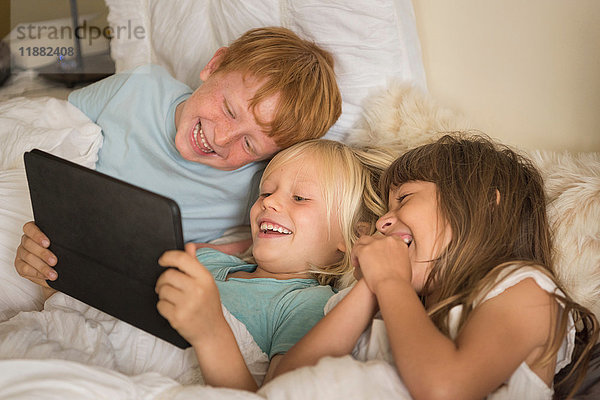 Kinder liegen im Bett und schauen auf das digitale Tablett