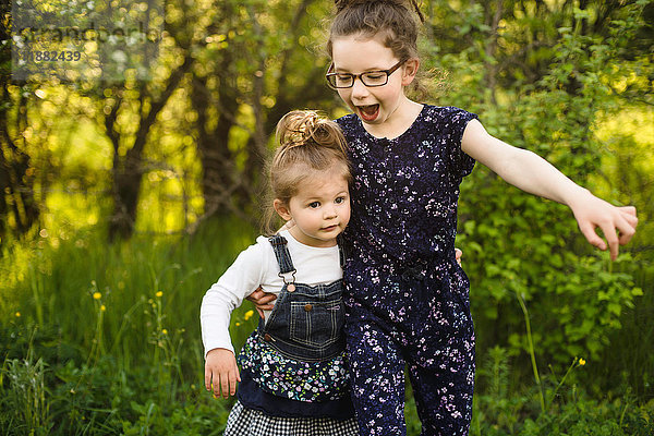 Mädchen und kleine Schwester spielen auf einem Feld mit Bäumen