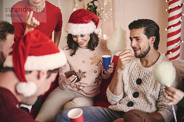 Junge Frauen und Männer sehen auf der Weihnachtsfeier ein Smartphone auf dem Sofa