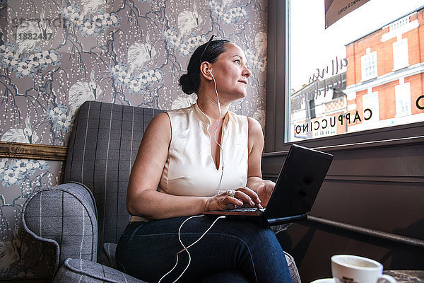 Geschäftsfrau in Kaffeebar schaut mit Laptop durchs Fenster