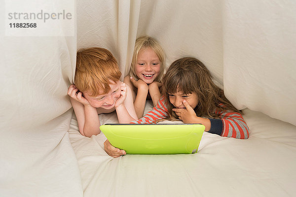 Kinder liegen im Bett und schauen auf das digitale Tablett