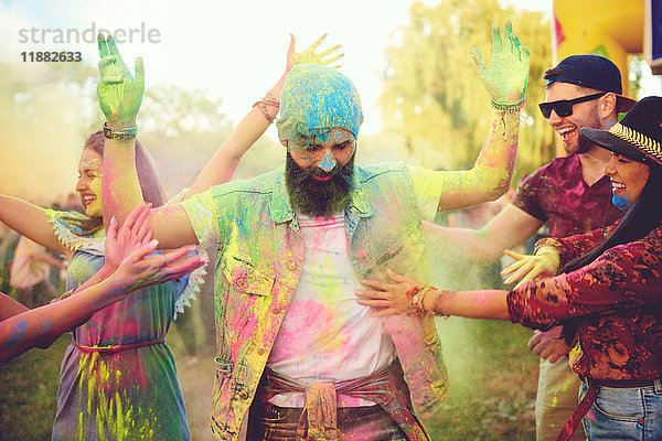Junge erwachsene Freunde werfen mit farbigem Kreidepulver und tanzen auf dem Festival