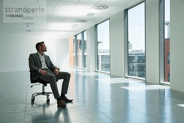 Geschäftsmann sitzt auf einem Stuhl in einem leeren Büro und schaut aus dem Fenster