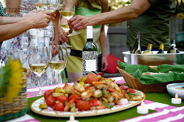 Personengruppe beim Gartenfest  Weingläser halten  Toast ausbringen  Essen auf dem Servierteller im Vordergrund  Mittelteil