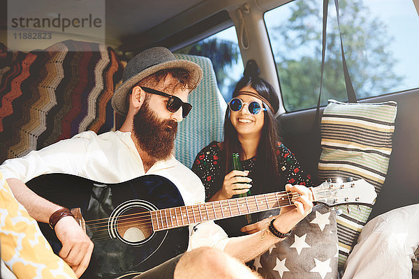 Junges Boho-Paar spielt Akustikgitarre im Wohnwagen