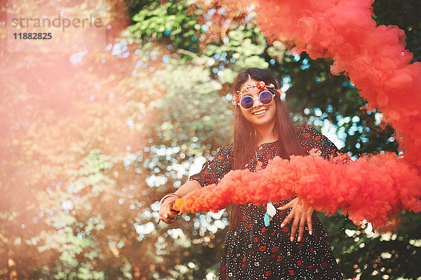 Junge Boho-Frau tanzt mit roter Rauchfahne auf dem Festival