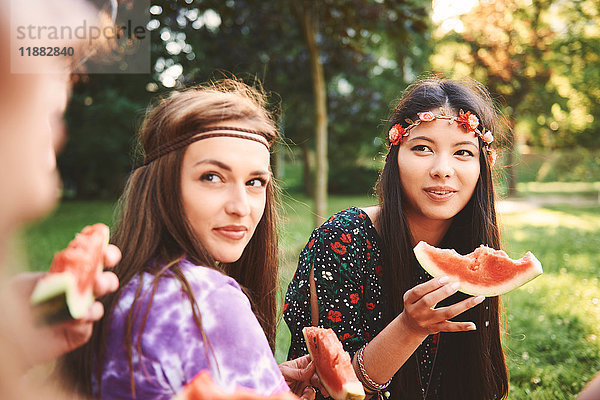 Junge Boho-Frauen essen Melonenscheibe beim Festival