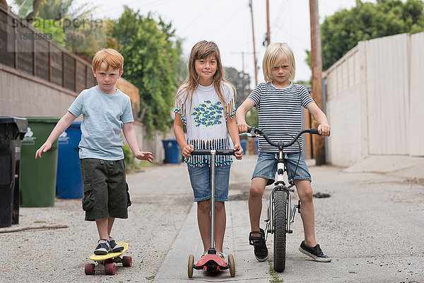 Mädchen und Jungen in der Spur mit Roller  Fahrrad und Skateboard