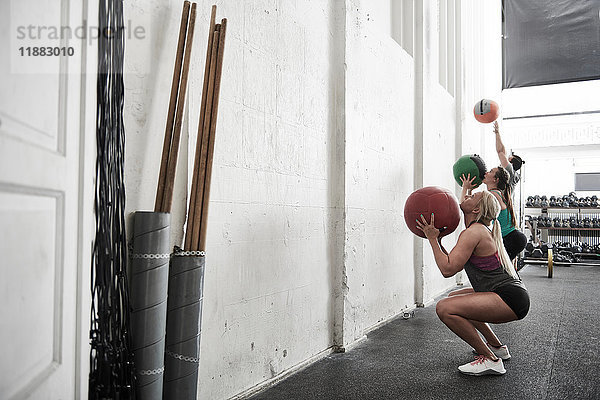 Freunde werfen Fitnessball gegen die Wand in einer Cross-Trainingshalle