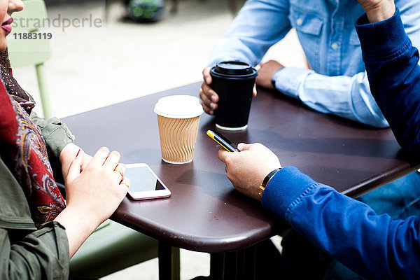 Ausschnitt von Freunden mit Smartphone beim gemeinsamen Kaffeetrinken