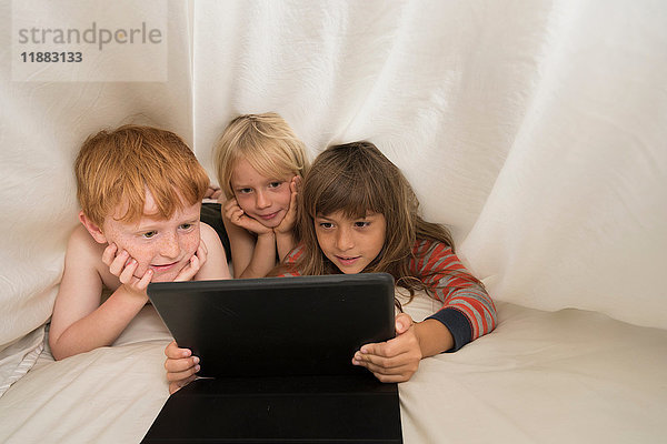 Kinder liegen im Bett und schauen auf das digitale Tablett