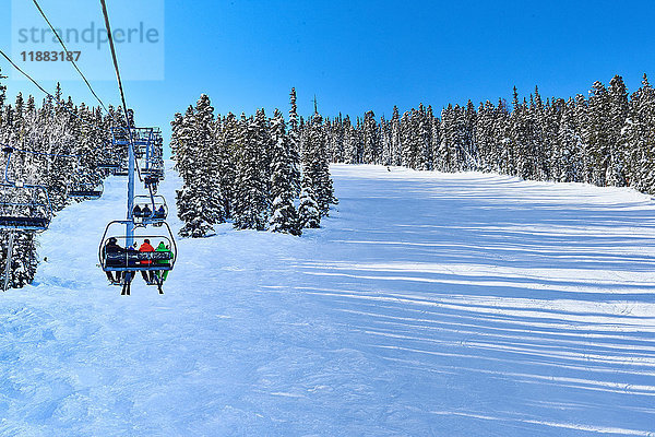 Rückansicht von Skifahrern auf einem Skilift  die sich in einer verschneiten Landschaft fortbewegen  Aspen  Colorado  USA