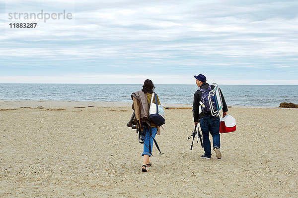 Rückansicht eines jungen Paares mit Seefischfangausrüstung am Strand