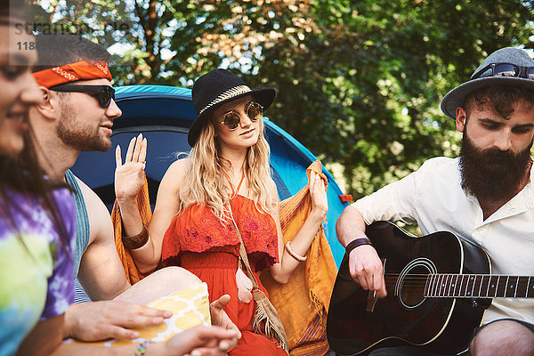 Junge erwachsene Freunde spielen Akustikgitarre beim Festival-Camping