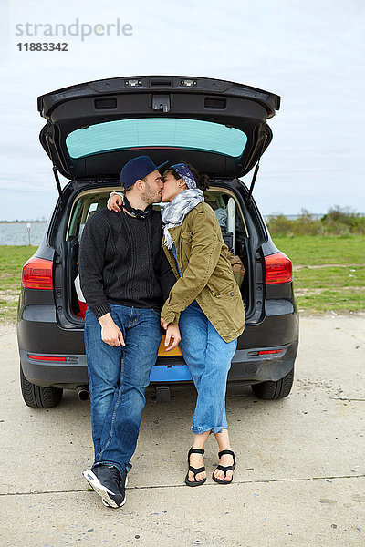 Junges Paar sitzt im offenen Kofferraum und küsst sich