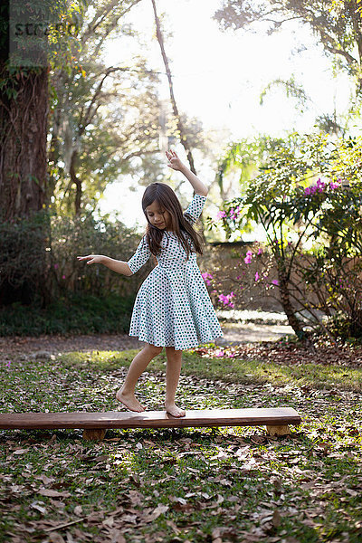 Mädchen balanciert auf einer Holzstufe im schattigen Garten