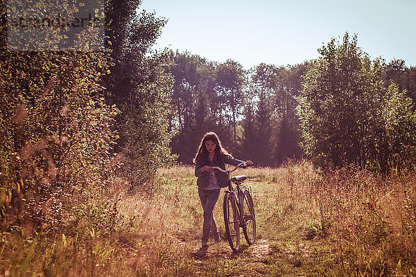 Mädchen schiebt Fahrrad im Feld