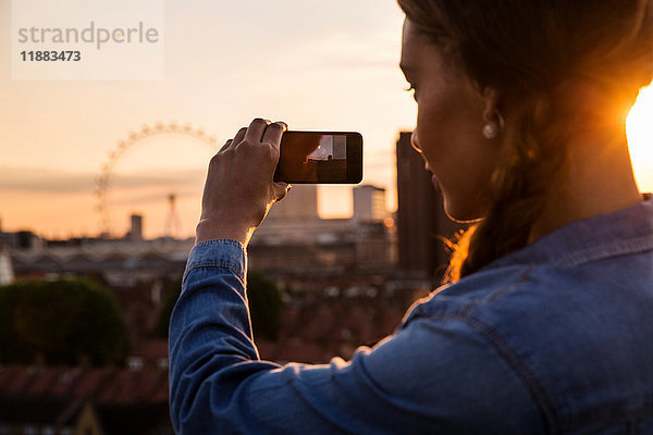 Junge Frau fotografiert Skyline bei Sonnenuntergangs-Dachparty in London  Großbritannien