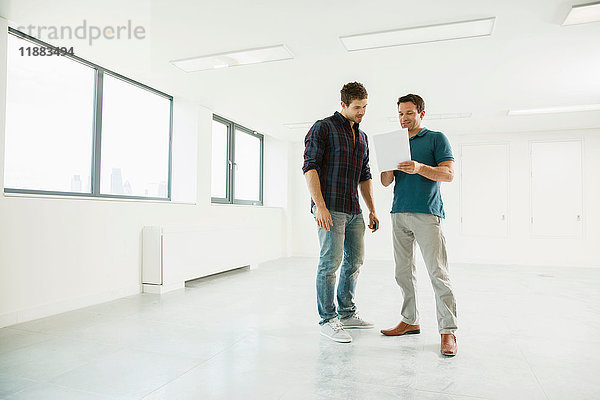 Zwei Männer stehen in einem leeren Büro und schauen auf ein digitales Tablet
