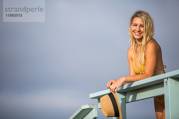 Porträt einer jungen Frau in Bikini-Oberteil  die sich an den Balkon einer Strandhütte lehnt  Santa Monica  Kalifornien  USA