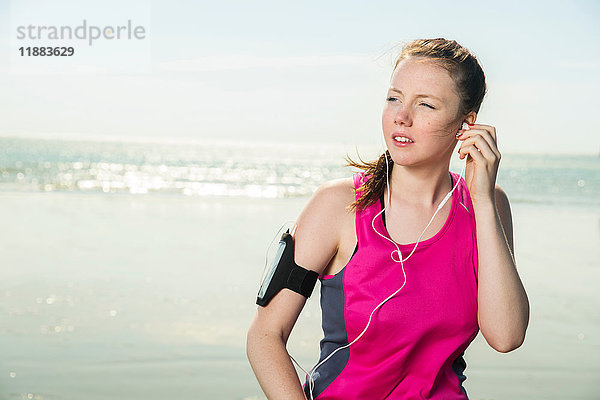 Junge Frau mit Kopfhörern am Strand beim Einstellen der Musik auf der Armbinde  Folkestone  UK
