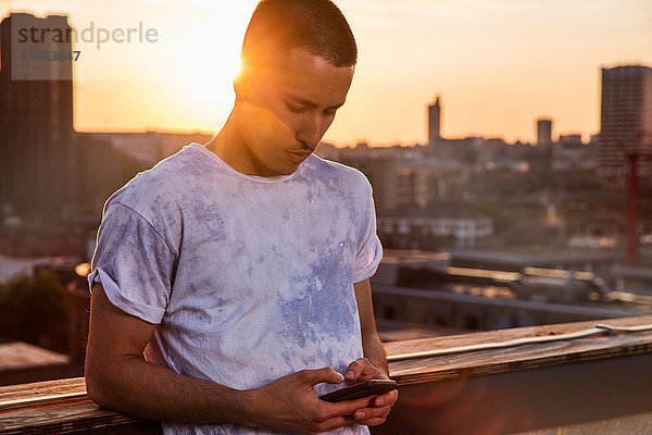 Junger Mann betrachtet Smartphone auf Sonnenuntergangs-Dachparty in London  Großbritannien