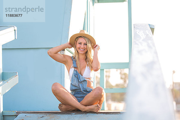 Porträt einer jungen Frau mit gekreuzten Beinen auf einer Strandhütte  Santa Monica  Kalifornien  USA